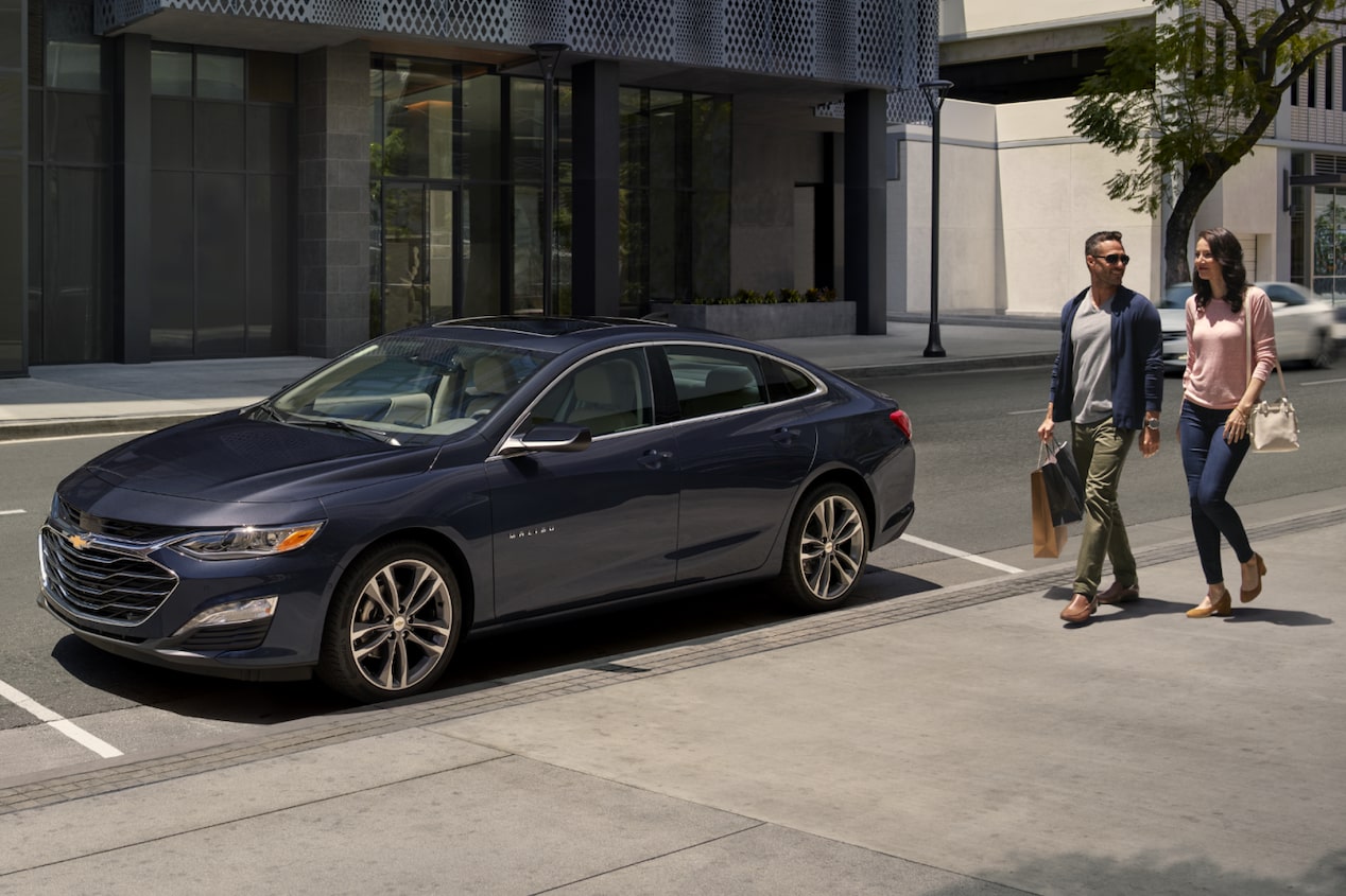 Front Side View of Lakeshore Blue Metallic 2025 Chevy Malibu Parked with Two People Behind It