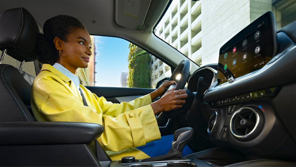 A Woman Driving a Chevy Vehicle While In-Vehicle Apps are Displayed on the Touchscreen