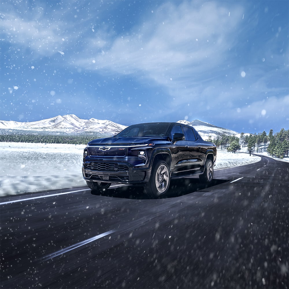 A Chevy Silverado EV Driving Down a Road with Snowy Mountains in the Background