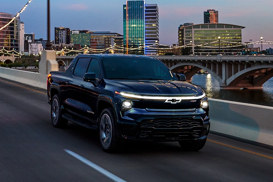 Three-Quarters View of a Black 2025 Chevrolet Silverado EV Driving Down the Road Under the Night Sky