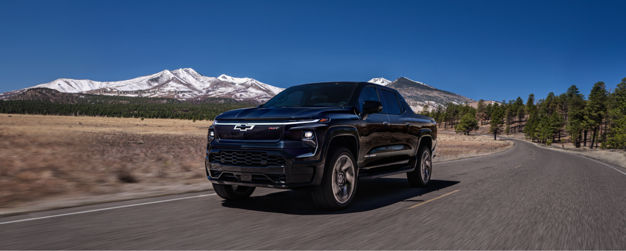 2024 Chevy Silverado EV Driving Down A Road With  Mountains In The Background