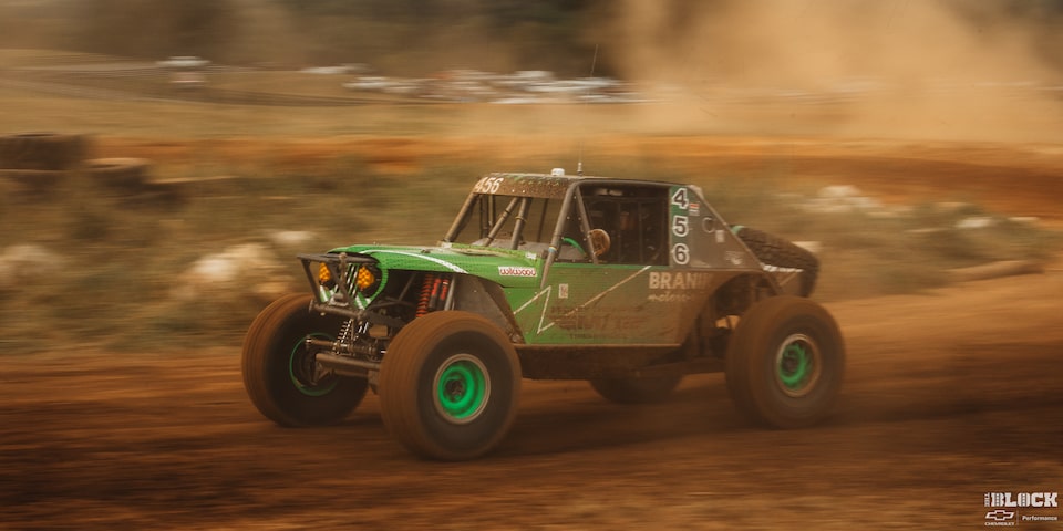 Side View of a Green Off-Road Vehicle Speeding Down the Trail with Dust Coming from Behind