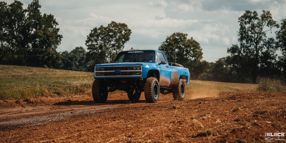 Three Quarters View of a Blue Chevy Pickup Truck Driving Down a Dry Trail