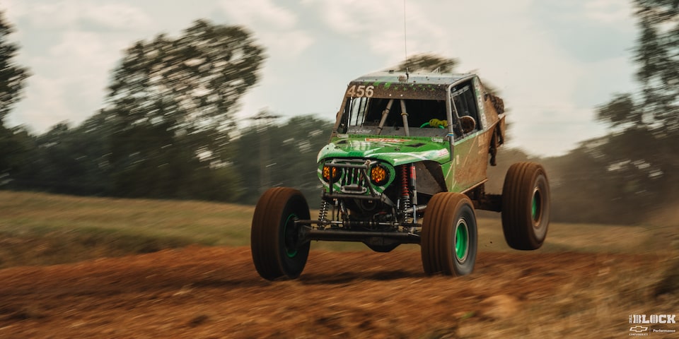 Three Quarters View of a Green Custom Off Road Vehicle Jumping Forward with the Rear Lifted Upward as Its Speeding Ahead